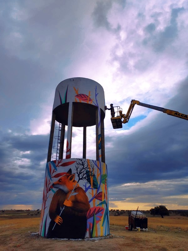 artiste sur la nacelle d'une grue peignant une fresque sur un batiment industriel